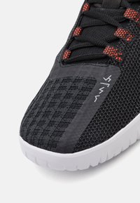 Sort sportsko med en struktureret mesh-overdel, orange detaljer og en hvid gummisål med et markant mønster.