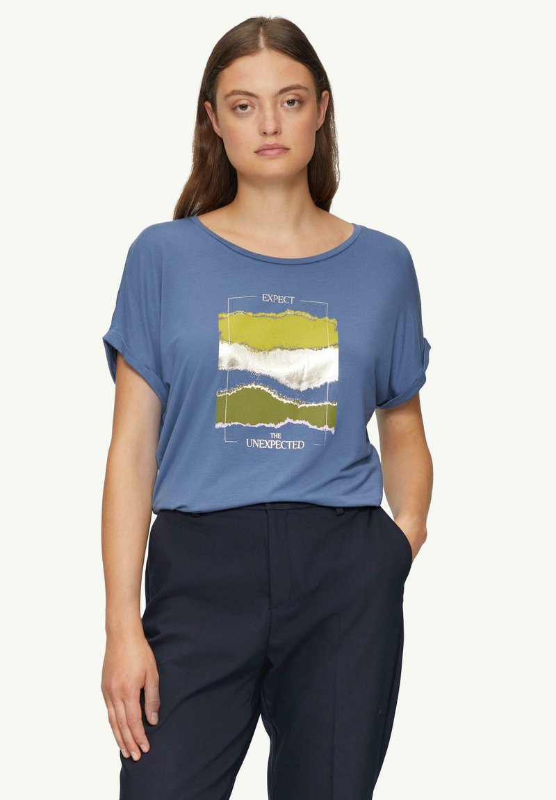 Niebieska koszulka z krótkim rękawem z graficznym wzorem zawierającym pasy w kolorach zielonym, białym i niebieskim oraz napis "OCZEKUJ NIEOCZEKIWANEGO."