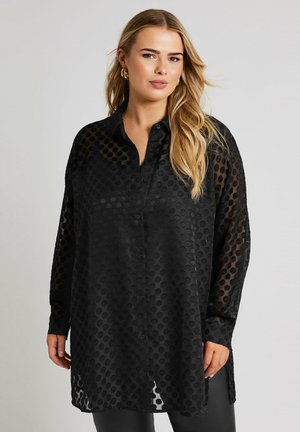 Camicia nera con bottoni realizzata in tessuto trasparente con motivi circolari. Presenta un colletto aperto e maniche lunghe con polsini abbottonati.