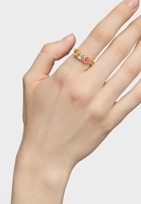 Złoty metalowy pierścionek z trzema kolorowymi kamieniami szlachetnymi: jasnoniebieskim, różowym i zielonym. Wzór obejmuje kwiatowe kształty wokół kamieni.