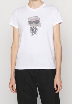 Camiseta de algodón blanca con un diseño gráfico negro de un personaje con gafas de sol y traje. Mangas cortas y estilo de cuello redondo.