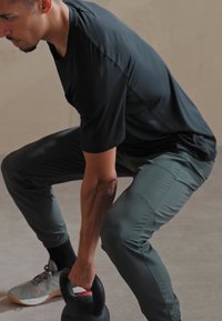 Czarny, krótki rękaw sportowy T-shirt oraz szare, tapered spodnie. Osoba unosi kettlebell. Minimalistyczny design, lekki materiał, dopasowany krój.