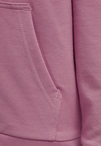 Lichtroze sweatshirtstof met een gladde textuur, voorzien van een zijzak en gestikte naden voor structuur. Eenvoudig en functioneel ontwerp.