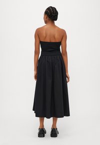 Svart strapless kjole med tettsittende overdel og en utsvingt, ankel-lang skjørt. Stoffet virker glatt med en lett glans. Ingen synlige mønstre.