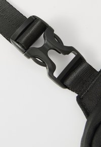 Gros plan sur une boucle noire et durable fermant une sangle, avec un tissu texturé, sur fond blanc.