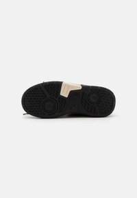 Semelle de chaussure noire en caoutchouc avec des motifs texturés, dotée d'un accent crème. Comprend des détails de grip circulaires et en zigzag.