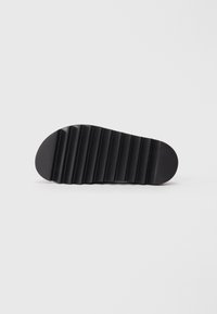 Black rubber sole featuring a ridged, textured design with a rounded toe and a smooth, flat surface.