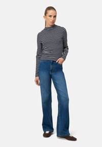 Pruhované tričko s dlhým rukávom v čiernej a bielej farbe, skombinované s modrými širokými džínsami. Rifle majú vysoký pás a minimálny švový detail.