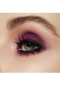 Close-up van een oog met een gradient van paarse oogschaduw met een matte afwerking, dikke wimpers en een subtiele glans rond het ooglid.