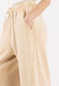 Beige, myke joggebukser i stoff med elastisk midje, snor og sidelommer. Har detaljer i sidesøm og en avslappet passform.