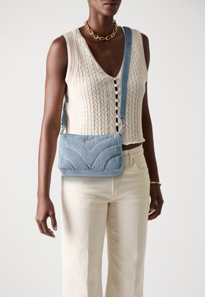 Torba crossbody z denimu w jasnoniebieskim kolorze, z pikowanym wzorem, srebrnymi akcentami i regulowanym paskiem. Torba ma smukły, prostokątny kształt.