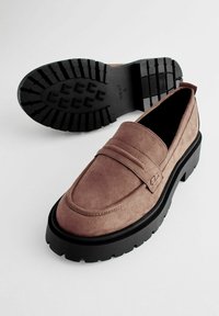 Mocassini in suede marrone con suola in gomma nera, presentano un tradizionale dettaglio a tasca per monete e un design con punta arrotondata.