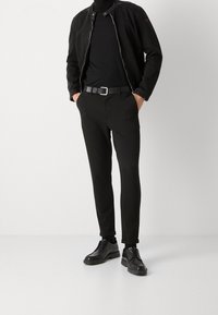 Czarna skórzana kurtka na czarnym golfie, zestawiona z dopasowanymi czarnymi spodniami i czarnymi sznurowanymi butami. Minimalistyczny design o gładkich liniach.