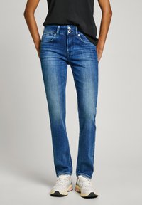 Jeans en denim bleu clair avec une coupe ajustée, présentant une texture lisse, deux poches avant et une braguette avec deux boutons visibles.