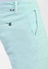 Lichtblauwe katoenen broek met een gladde textuur, voorzien van zijzakken, een klein logotag en accentstiksel langs de tailleband.