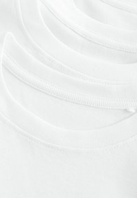 T-shirts en coton blanc empilés, avec des cols ronds côtelés, une texture lisse et des détails de couture subtils le long de l'encolure.