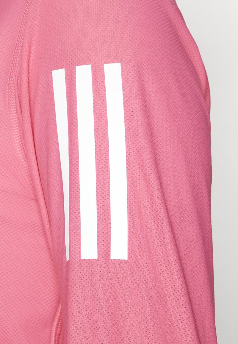 Rosa Sportshirt aus strukturiertem Material, mit drei weißen Streifen am linken Ärmel. Leichtes, atmungsaktives Design.