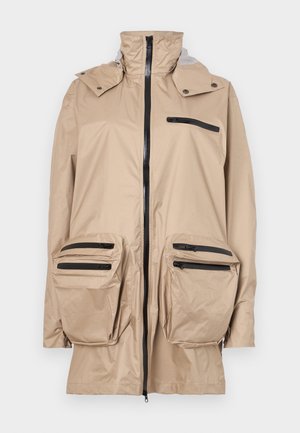 Beige wasserdichte Jacke mit hohem Kragen, frontalem Reißverschluss und mehreren schwarzen Reißverschlusstaschen auf der Brust und den Hüften. Glatte Textur.