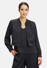 Zwarte satijnen cropped jack met een ronde hals, lange mouwen en elastische manchetten, gedragen over een bijpassend topje. Soepele textuur, minimalistisch ontwerp.