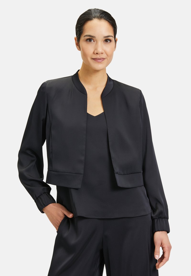 Zwarte satijnen cropped jack met een ronde hals, lange mouwen en elastische manchetten, gedragen over een bijpassend topje. Soepele textuur, minimalistisch ontwerp.