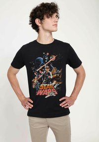 T-shirt en coton noir avec un graphique coloré de style rétro présentant des personnages et des éléments de Star Wars, avec du texte en bas.