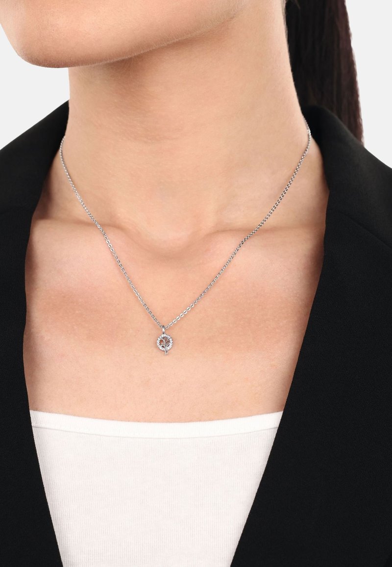 Silverhalsband med ett bladformat hänge, prytt med en klunga av små stenar, fäst vid en tunn kedja. Bärs över en vit topp.