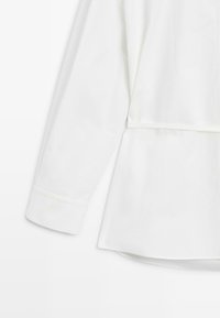 Wit shirt met lange mouwen en een iets losse pasvorm, voorzien van manchetten bij de polsen, een band aan de taille en een zachte katoenen stoftextuur.