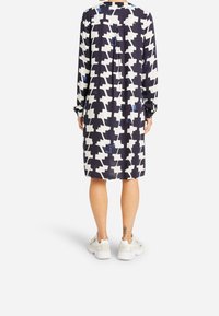 Námořnické šaty s bílým a modrým abstraktním vzorem, dlouhými rukávy a knoflíkovými manžetami, v kombinaci s bílými teniskami. Hladká textilie.