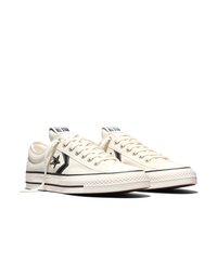Een paar crèmekleurige Converse lage sneakers met een zwart sterrenlogo en witte veters op een witte achtergrond.