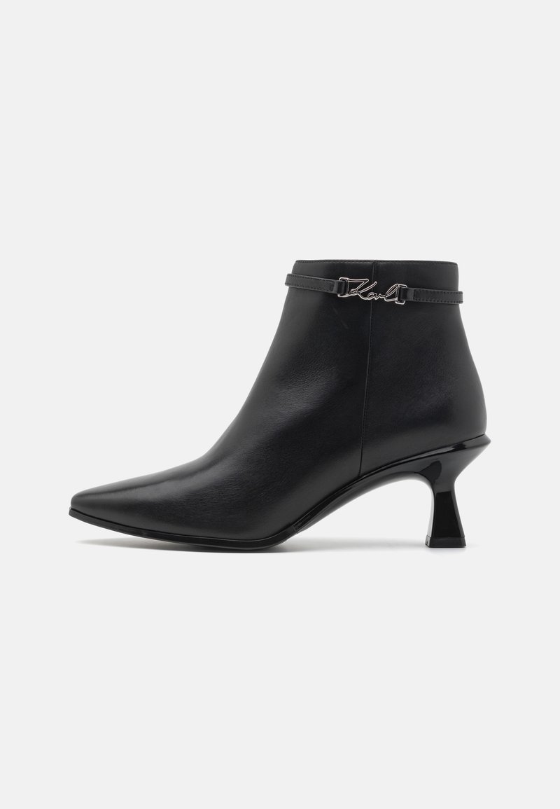 Botte noire en cuir à cheville avec bout pointu, talon kitten, et une fine lanière ornée d'une boucle décorative argentée.