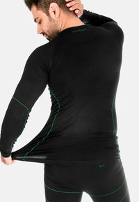 Schwarzes, athletisches Langarmshirt mit grüner Akzentnaht, das über eine strukturierte Paneelierung auf dem Rücken und ein eng anliegendes Design verfügt.