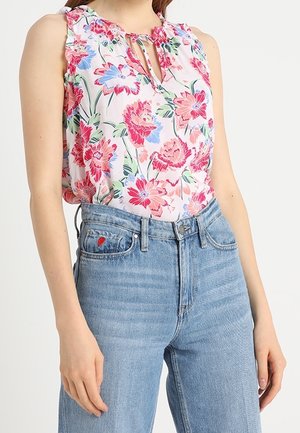 Bezrekawnikowa bluzka w kwiaty w różowym, czerwonym i niebieskim kolorze, zestawiona z jasnoniebieskimi dżinsami z wysokim stanem, na kieszeni znajduje się małe czerwone serce.