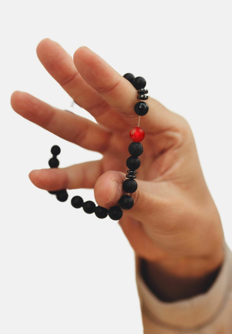 Perlas negras con un acento rojo, ensartadas, sostenidas entre los dedos. Incluye separadores metálicos negros entre las perlas.