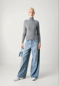 Camisola cinza de manga longa com gola alta combinada com jeans de perna larga de cintura alta em azul claro, acessorizada com uma pequena mala azul e ténis brancos.