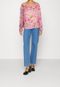 Blouse rose à fleurs avec épaules dénudées et encolure à volants, associée à un jean bleu droit et des chaussures plateformes noires.