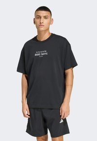 Schwarzes T-Shirt mit kurzen Ärmeln und weißem "ADIDAS TRAINING"-Text, aus weichem Stoff gefertigt, kombiniert mit schwarzen Shorts mit weißem Logo.