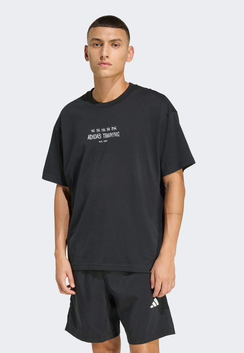 Schwarzes T-Shirt mit kurzen Ärmeln und weißem "ADIDAS TRAINING"-Text, aus weichem Stoff gefertigt, kombiniert mit schwarzen Shorts mit weißem Logo.