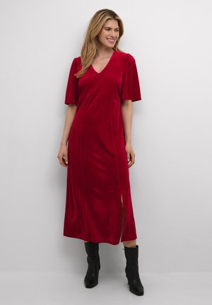 Rode fluwelen midi-jurk met korte pofmouwen, V-hals, zijsplitten en een gladde textuur. Draagt met zwarte enkelbootjes voor contrast.