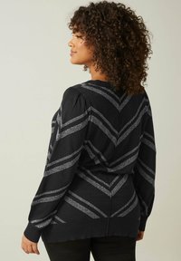 Maglione nero con strisce a zigzag argento metallizzato, maniche a palloncino e una texture morbida. Presenta un collo a giro e un retro leggermente più lungo.