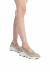 Zapatos color beige tipo slip-on con parte superior de malla, acentos metálicos y una suela de cuña de goma blanca. Punta redondeada con sutiles detalles de costura.