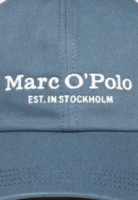 Casquette de baseball en coton bleu avec un texte brodé en blanc "Marc O'Polo" et "EST. À STOCKHOLM" à l'avant. Visière structurée, tissu texturé.