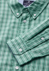 Green plaid button-up shirt with contrasting white and dark green lines, featuring a collar and white buttons on the front and cuffs.