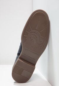 Námořnické tenisky s texturovaným svrškem a gumovou podrážkou. Spodní část má vzor se zvýrazněním sochy Svobody a značkový nápis "TOMMY HILFIGER".