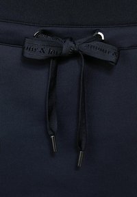 Navy blue urheilusortsit, joissa on teksturoitu vyötärönauha, logopainettu naru ja metalliset päätypistokkeet narun päissä.