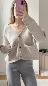 Svijetlosmeđi pleteni kardigan s V-izrezom, dugim rukavima, rebrastim manžetama i dva prednja džepa, s tamnim dugmadi za zatvaranje.