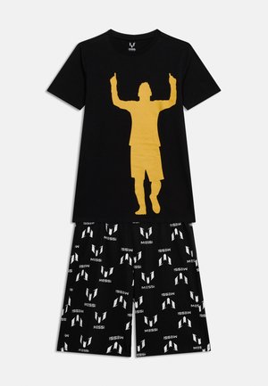 Cămașă neagră cu mânecă scurtă, cu o siluetă aurie a unui jucător de fotbal ridicând ambii degete arătători, asortată cu pantaloni scurți negri cu model de sigle albe "MESSI".