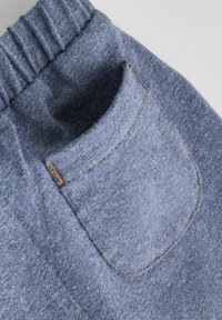 Tissu bleu chiné avec une texture douce, présentant une taille élastique et une seule poche au dos cousue avec du fil orange.