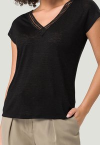 Svart kortärmad topp med V-ringning och dekorativt virkat kantband. Tillverkad av ett lätt tyg, med en avslappnad passform och mjuk textur.