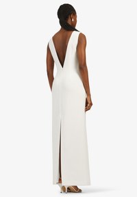 Robe blanche longue jusqu'au sol avec un dos en V profond, une silhouette ajustée et une haute fente latérale ; texture lisse et design minimaliste.