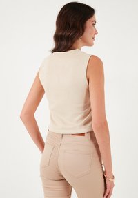Beige top bez rukávů s hladkým povrchem, kulatým výstřihem a přiléhavým střihem, spárovaný s světlými béžovými džínami s vysokým pasem.
